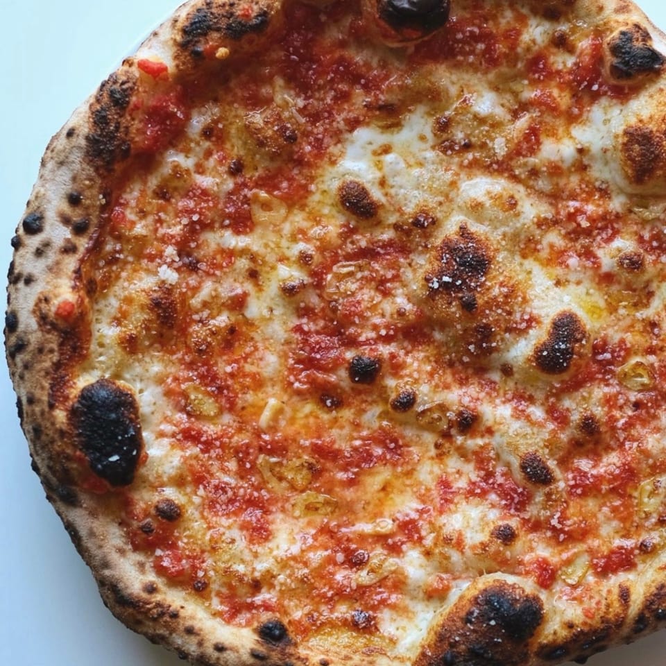 Close-up of a Warrior New York Pizza with bubbly crust, melted cheese, and red sauce.