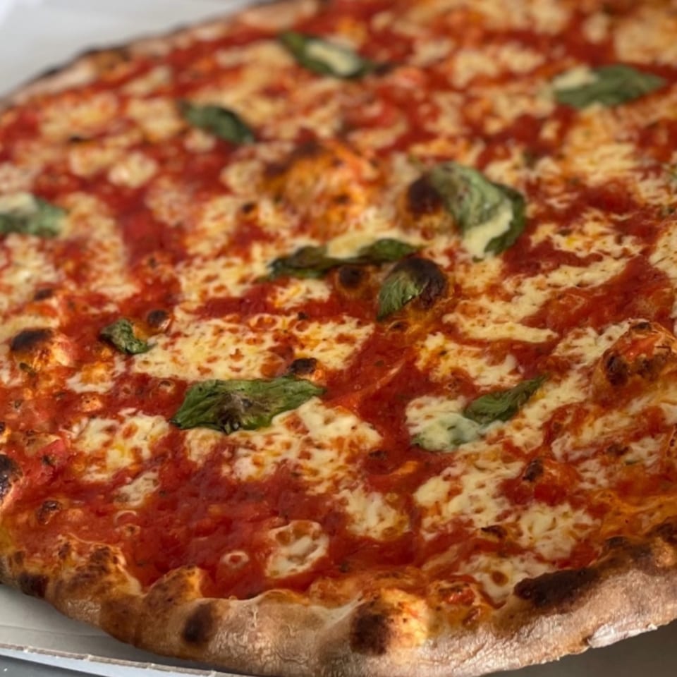 A close-up of a Warrior New York Pizza Margherita, with melted cheese, red sauce, and basil.
