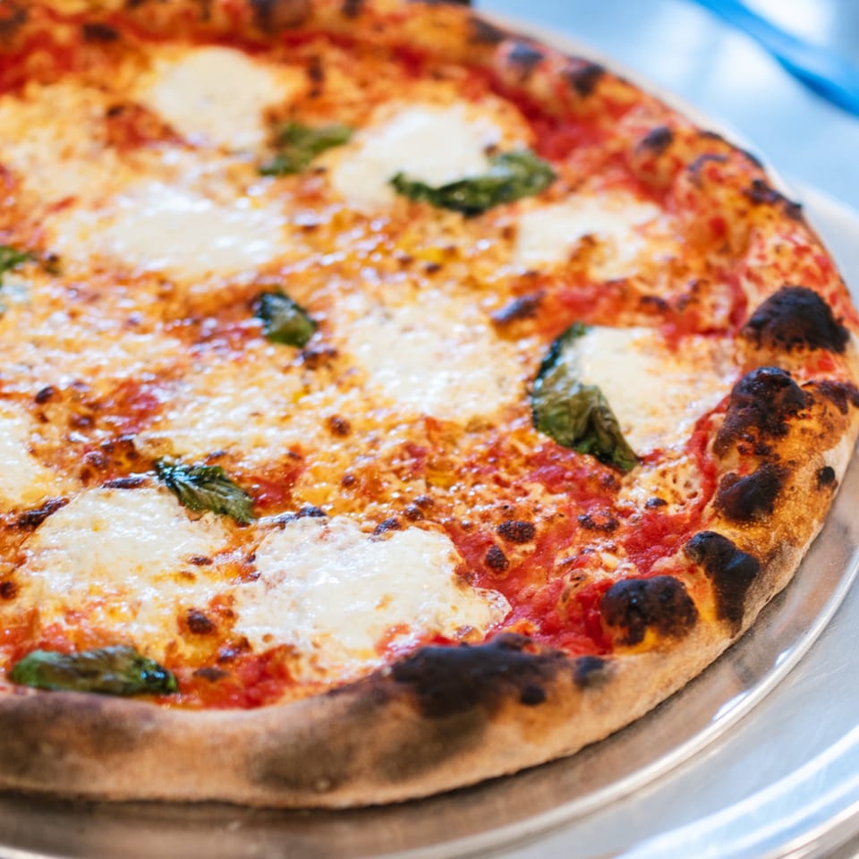 Close-up of a Warrior New York Pizza Margherita pizza with fresh mozzarella, basil, and charred crust.