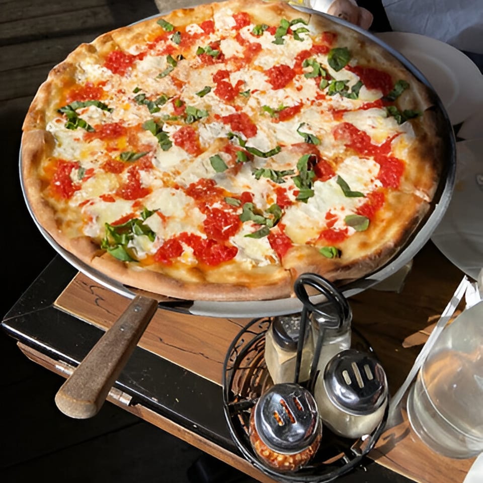 A large, round Warrior New York Pizza with red sauce, white cheese, and fresh basil.