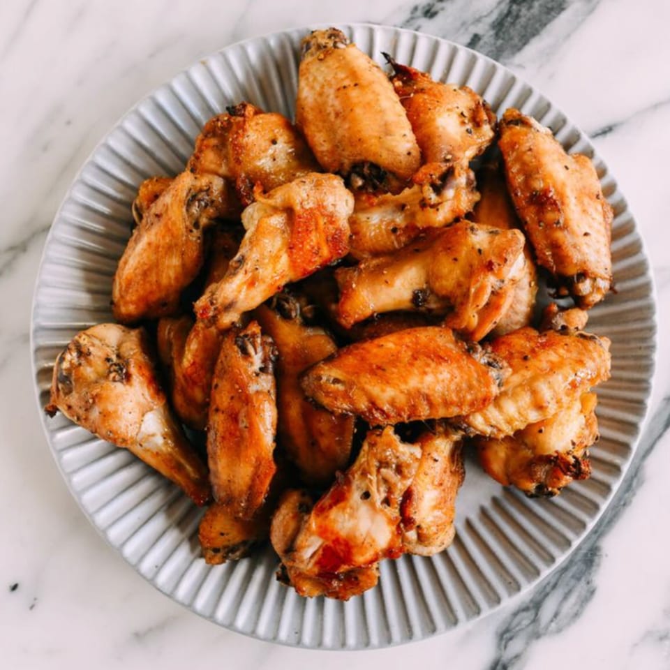 A plate of crispy, golden-brown chicken wings, seasoned with pepper, from Warrior New York Pizza.