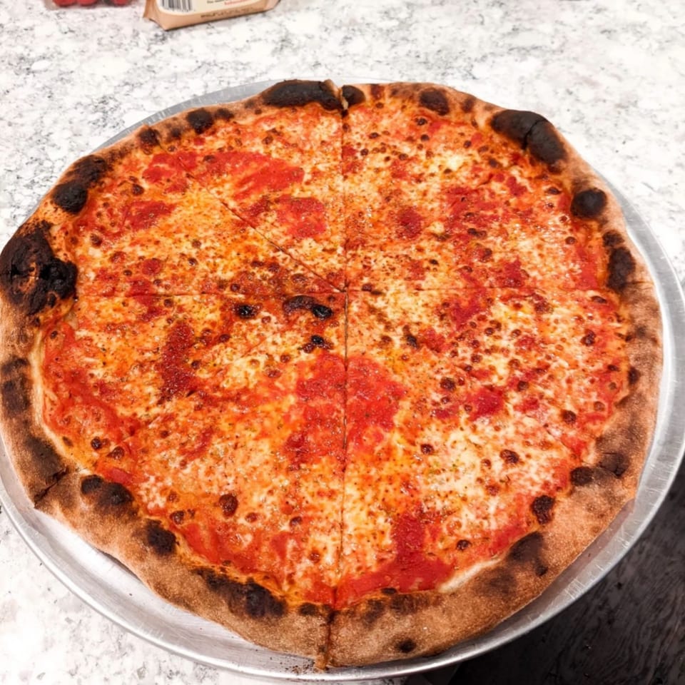 A whole Warrior New York Pizza, sliced into eight pieces, on a metal tray.