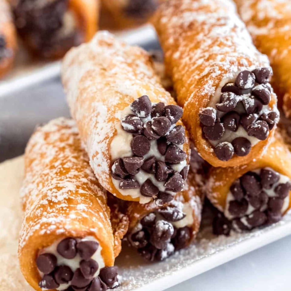 Close-up of several Warrior New York Pizza cannolis, filled with cream and chocolate chips, dusted with powdered sugar.