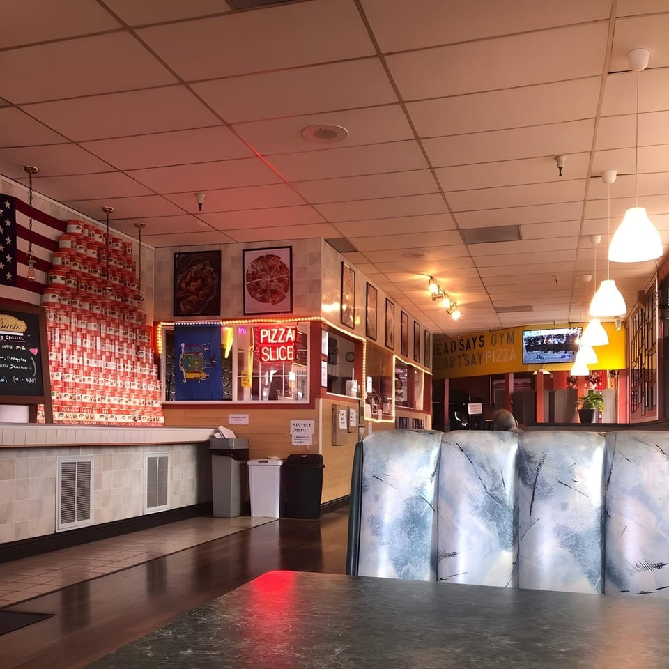 Interior of Warrior New York Pizza, showing dining area with booths, American flag decor, and a "Pizza Slice" sign.