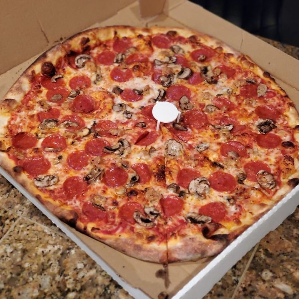 A Warrior New York Pizza with pepperoni, mushrooms, and sausage in a cardboard box.