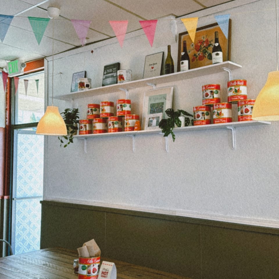 Interior of Warrior New York Pizza with shelves of tomato cans, wine bottles, and colorful bunting.