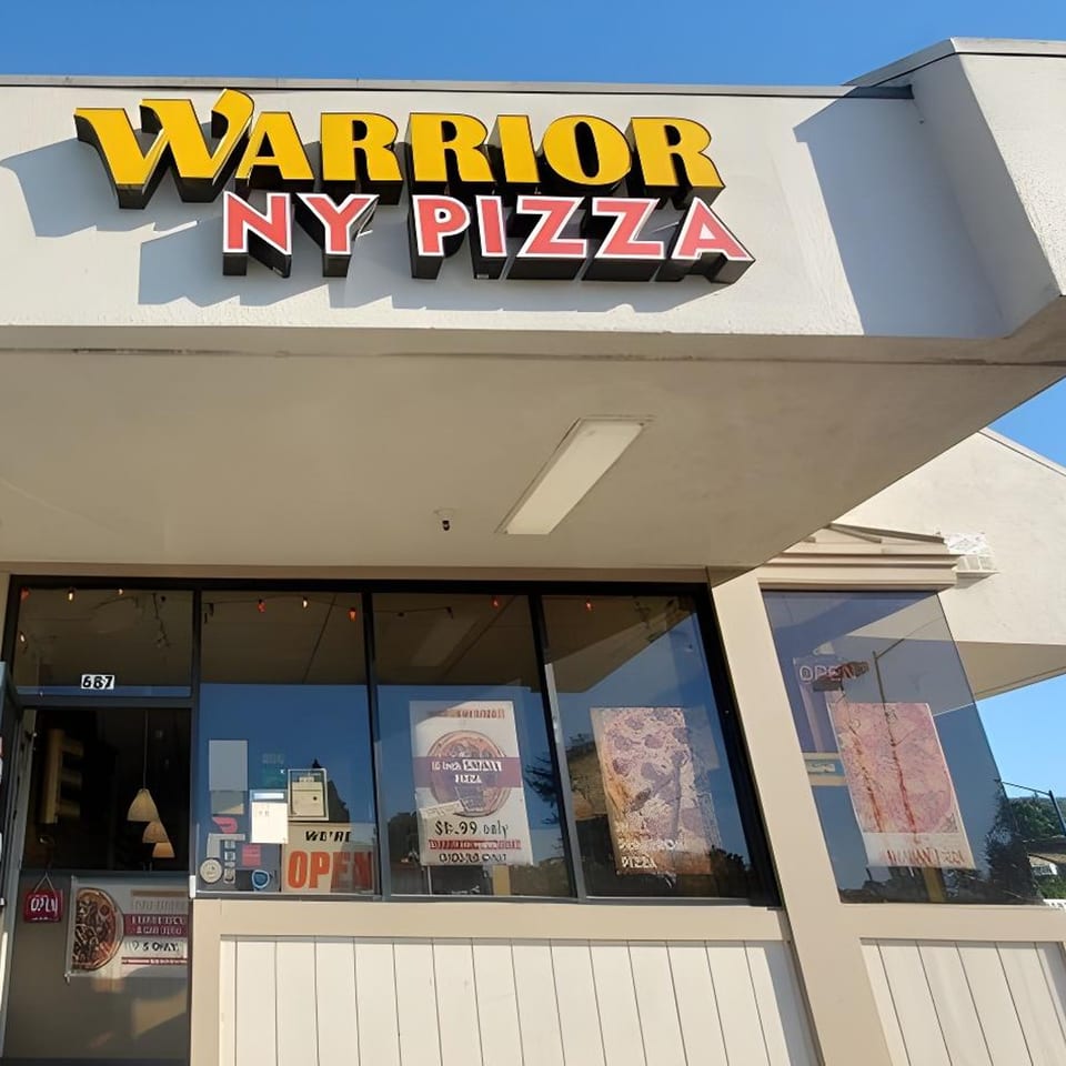 Exterior of Warrior New York Pizza with a yellow and red sign and window advertisements.